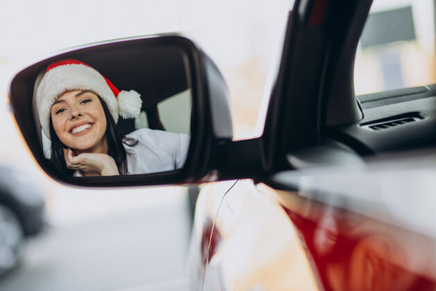 红帽圣诞节在汽车陈列室戴圣诞帽的女人车辆圣诞帽鞠躬