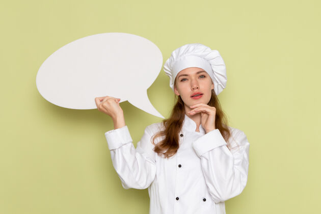 烹饪身穿白色厨师服的女厨师手持绿色墙上的白色标志思考衣服烹饪穿