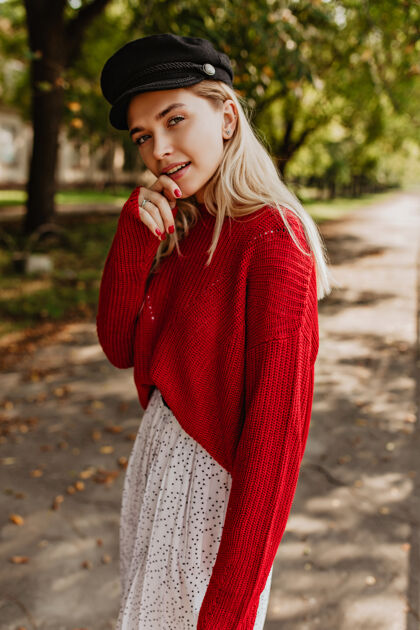 女人美丽的金发女郎在秋天的公园里摆姿势漂亮的女孩戴着漂亮的黑帽子 穿着红色毛衣和白色裙子漂亮瘦身华丽