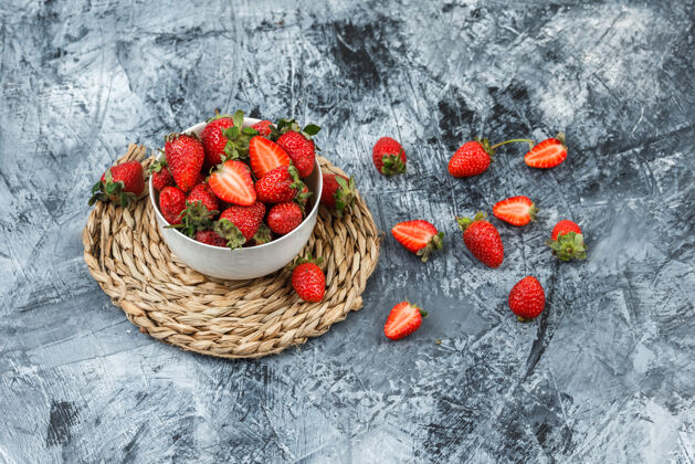 健康一碗草莓放在深蓝色大理石背景上的圆形柳条垫子上柳条维生素盘子