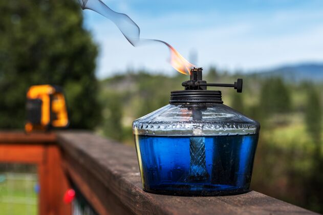 叶选择性聚焦拍摄放在水面和远处树木上的容器中燃烧的石油光明水金属