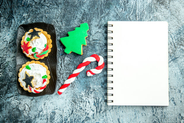 记事本上图：黑色盘子上的圣诞馅饼 灰色桌子上的圣诞糖果和圣诞树饼干记事本糖果笔记本圣诞树