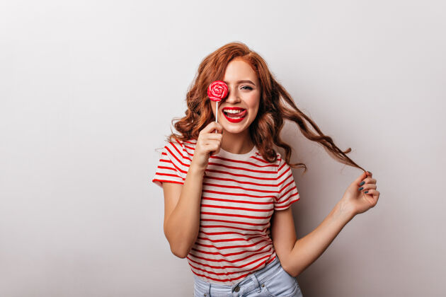 红发漂亮的女孩拿着糖果玩她的卷发优雅的长发女士和棒棒糖配件美味游戏
