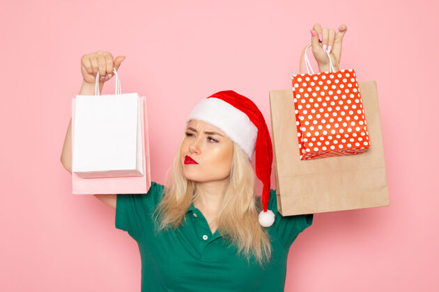 风景正面图年轻女性手持圣诞礼物在粉红色的墙上包装圣诞照片模型新年假期年轻女性美丽包装