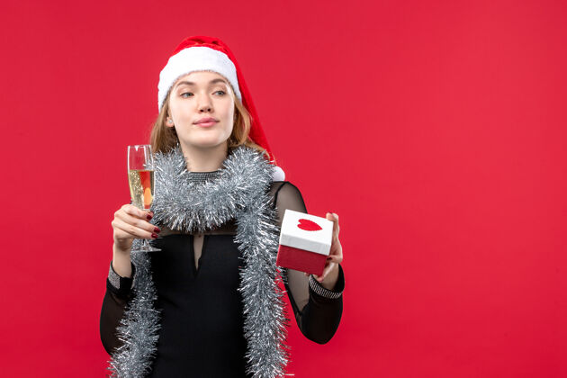 服装正面图年轻女性带着礼物在红墙上庆祝圣诞节圣诞新年年轻女性
