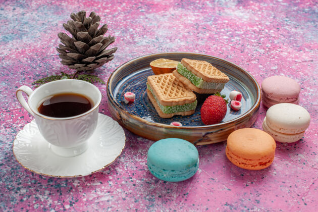 饮料美味的饼干三明治和美味的法国马卡龙和一杯茶放在粉红色的桌子上糖美味饼干