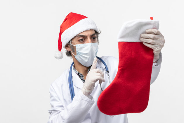 袜子正面图男医生拿着白色办公桌上的大节日袜子 病毒假日外套专家圣诞节