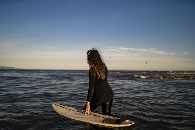 度假村浅焦拍摄的一个女性走在海边与冲浪板在她身边季节海岸线日落