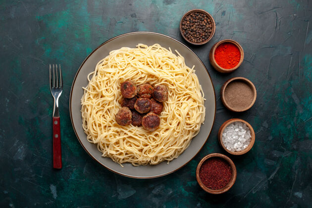 丸子顶视图煮熟的意大利面食与肉丸和调味品在深蓝色的表面肉意大利面食物