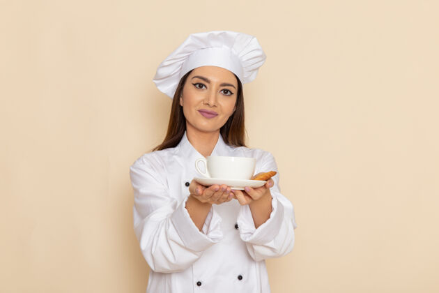 烹饪身穿白色厨师服的年轻女厨师正拿着一杯咖啡站在浅白的墙上咖啡帽子年轻