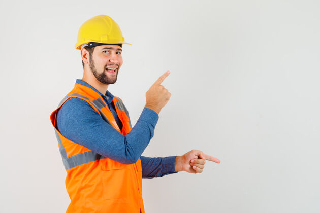 建筑年轻的建筑工人穿着衬衫 背心 头盔上下指指点点 看上去很高兴工作安全手指