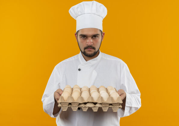 厨师年轻的男厨师穿着厨师制服 手里拿着一盒鸡蛋 在橙色的空间里显得孤立无援男性厨师持有