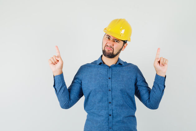 伙伴关系穿着衬衫 戴着头盔的年轻工人手指向上 看上去很不满意专业工程师存储