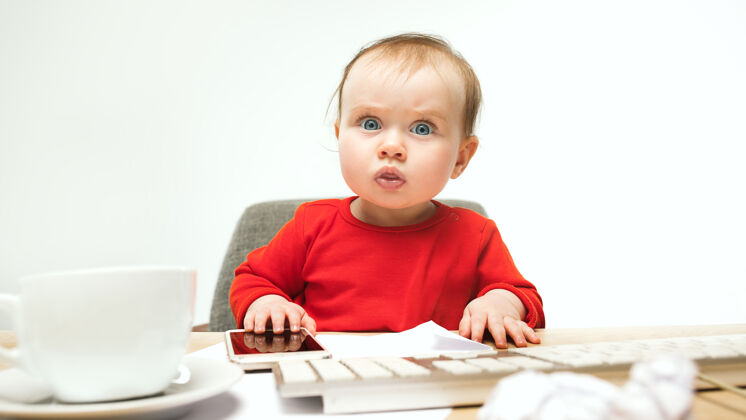 电脑第一条短信小女婴坐在键盘的现代电脑或笔记本电脑在白色办公桌乐趣惊喜