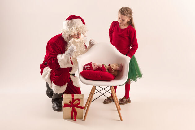 小可爱的新生小女婴和漂亮的妹妹穿着圣诞服装和圣诞老人的服装和帽子的男子圣诞画像乐趣宝贝红色
