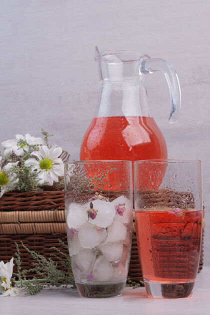 液体白桌子上放着新鲜的柠檬水和带雏菊的罐子玻璃篮子浆果