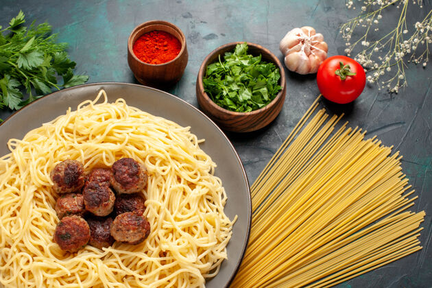 生的俯视图煮熟的意大利面食 深蓝色表面有肉丸和绿色菜肴球面食