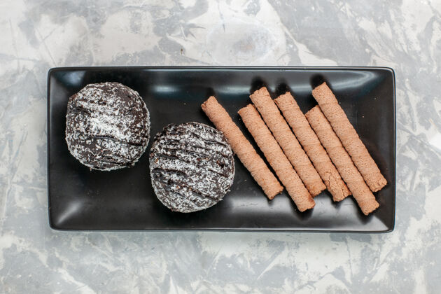 里面俯视图巧克力蛋糕与甜管饼干内的黑色盘子在白色的表面食物糖盘子