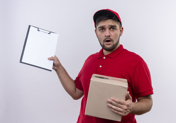 站着年轻的送货员穿着红色制服 拿着帽子的盒子 拿着一个用空白页写的剪贴板 看上去很困惑 很焦虑剪贴板帽子焦虑