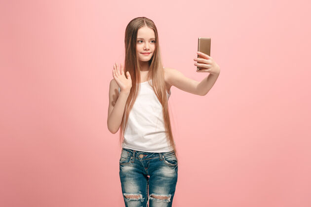 面部快乐的少女站着 粉色的微笑 用手机自拍人类的情感 面部表情的概念教育人乐趣
