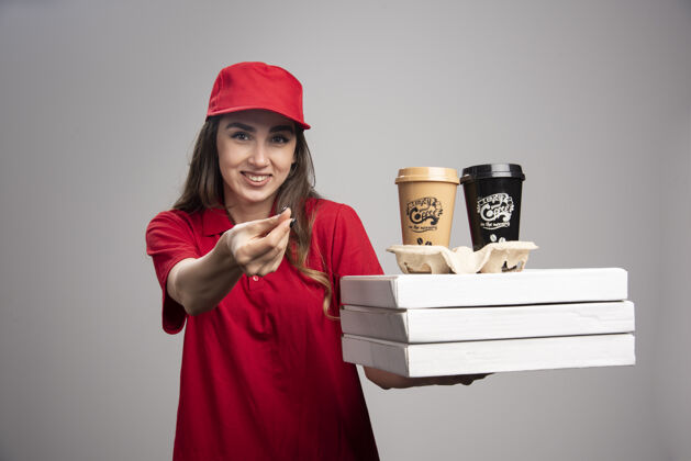 员工在灰色的墙上拿着比萨饼和咖啡杯的女服务员饮料咖啡承运人