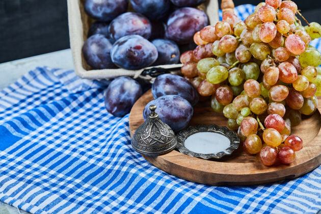 紫罗兰桌布上放着新鲜的李子和一串葡萄美味多汁成熟