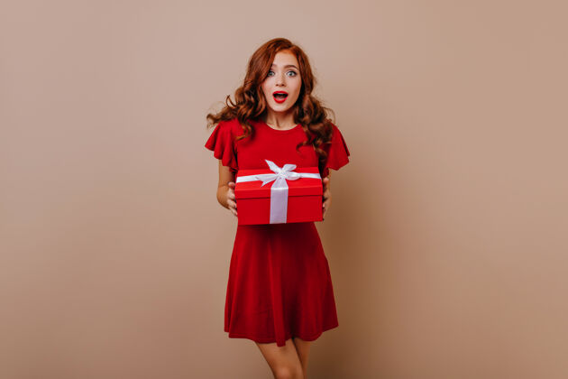 红发穿着红色短裙拿着礼物的惊喜女孩可爱的长发女人在准备新年礼物肖像快乐成人