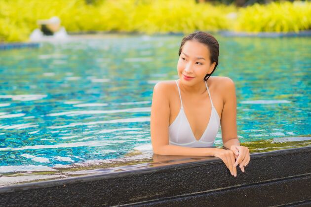 健康肖像美丽的亚洲年轻女子放松微笑休闲围绕室外游泳池近海享受放松度假