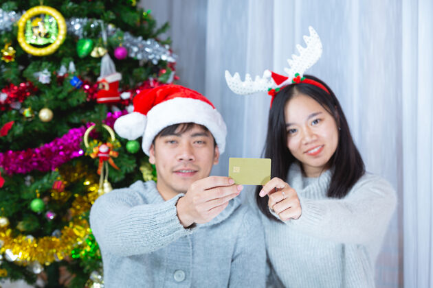 圣诞快乐戴着圣诞帽的情侣们一起拿着信用卡庆祝夏娃派对