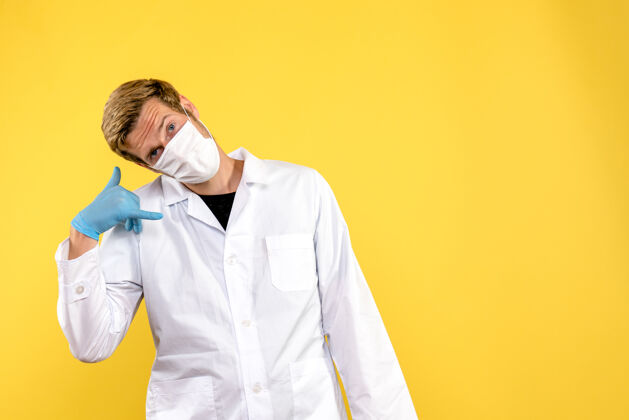 视图正面图男性医生戴着口罩在黄色背景上健康大流行的柯维病毒男性医生肖像外套