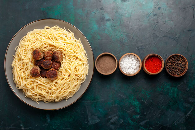 意大利顶视图煮熟的意大利面食与肉丸和调味品在深蓝色的表面一餐配料盘子