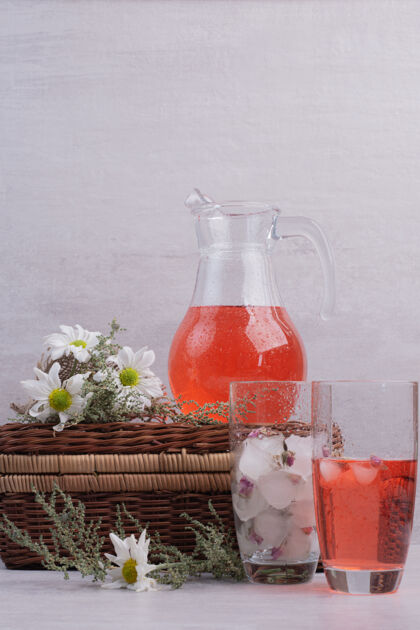 冰白桌子上放着新鲜的柠檬水和带雏菊的罐子浆果液体玻璃