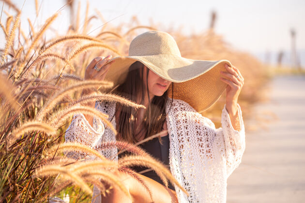 隐藏一个女人在阳光下的肖像 坐在田野里 穿着夏装 戴着帽子田野时尚阳光