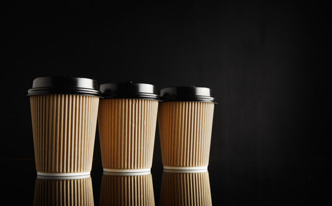 咖啡杯三个完全相同的浅棕色纸板外卖咖啡杯 黑色盖子排在靠着黑色墙壁的反光黑色桌子上Go茶商店