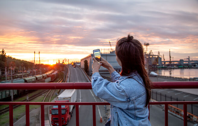 拍摄一位年轻女子用手机在桥上拍摄美丽的日落日落内容拍照