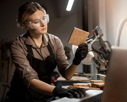 就业带着护目镜的女木匠在工作室里看着一块木头女性工作工作