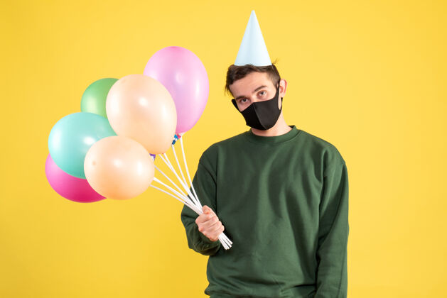 乐趣正面图：戴着派对帽 站在黄色地面上的彩色气球的年轻人气球人站着