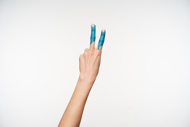 计数举起的女性手的肖像 显示两个手指涂成蓝色 同时形成胜利的姿态 被隔离在白色染色室内身体