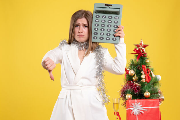 人正面图女医生站着拿着计算器 背景是黄色的圣诞树和礼品盒年微笑微笑