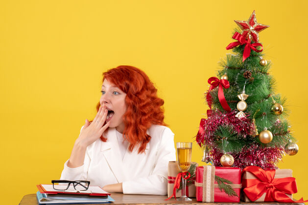 商务前视图：女医生坐在桌子后面 黄色背景上有圣诞礼物成人快乐微笑