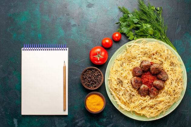 美味俯瞰美味的意大利面食与肉丸记事本和不同的调味品在深蓝色的背景午餐一餐面团