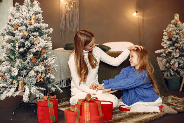 庆祝人们在为圣诞节做准备母亲在和女儿玩耍一家人在节日的房间里休息孩子穿着蓝色毛衣圣诞装饰女儿