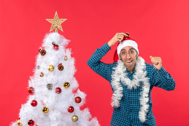 衬衫一个带着圣诞老人帽子 穿着蓝色条纹衬衫 满脸笑容 情绪化 滑稽可笑的年轻人圣诞老人年轻人圣诞树