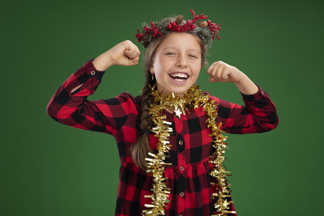 衣服戴着圣诞花环的小女孩穿着格子裙 脖子上挂着金属丝 高兴而兴奋地握紧拳头女孩花环小
