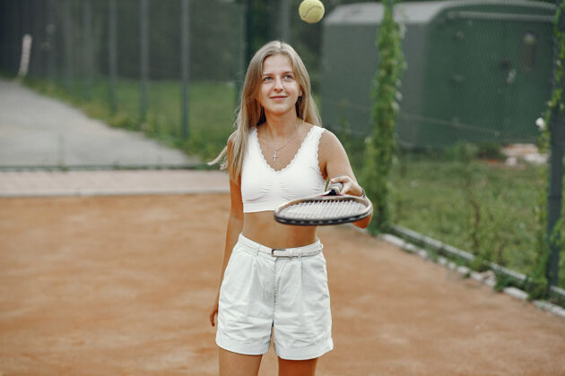 竞技今天玩得很开心 穿着t恤的年轻女子拿着网球拍和球的女子户外网嬉戏
