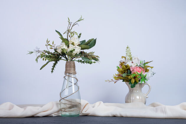 白色深色桌子上放着两瓶五颜六色的花叶花瓶桌布