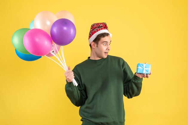 马拉卡正面图是一个戴着圣诞帽 站在黄色地面上的彩色气球的年轻人惊奇的年轻人欢乐飞机