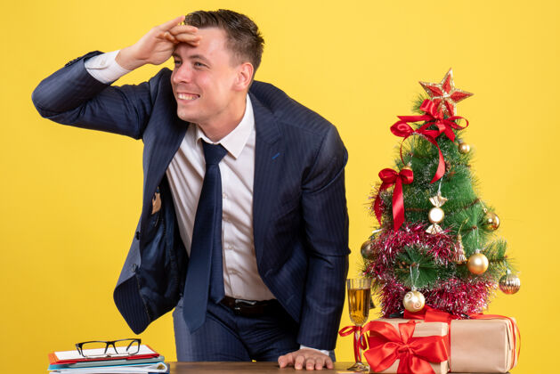 办公室圣诞树旁的快乐男人站在桌子后面 黄色的礼物商人男人新郎