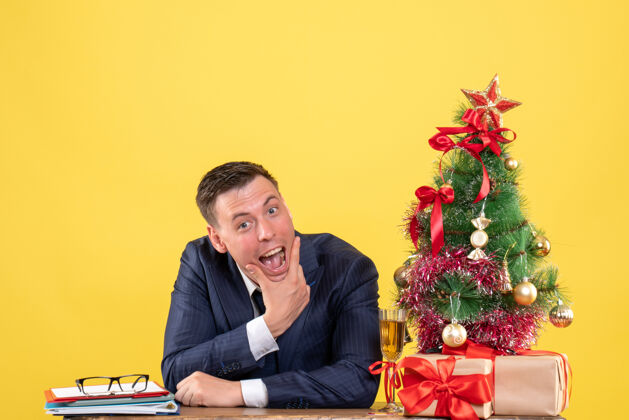 帅哥帅哥张嘴坐在圣诞树旁的桌子前 黄色的礼物坐着办公室嘴巴