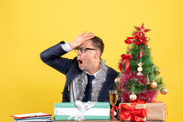 树失望的男人把手放在额头上 坐在圣诞树旁的桌子旁 用黄色表示礼物男人经理放